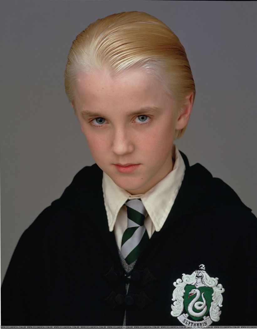 Harry Potter And The Philosopher`s Stone / Harry Potter Ve Felsefe Taşı Filmi - Draco Malfoy- Betimleyen: Sedef TAYLAN /  Boğaziçi Üniversitesi ED 200 Dersi Öğrencisi  Arka planı gri renkte olan dikey dikdörtgen şeklindeki fotoğrafın ortasında Draco Malfoy (Tom Felton), kafasını hafif eğip gözlerini yukarı kaldırmış bir bakışla yüzü dönük poz vermiş.  Draco, 11 yaşlarında bir oğlan çocuğu. Parlak, açık sarı saçları düz bir biçimde arkaya doğru taranmış. Uzun, ince bir yüzü var. Kafası hafif yana eğik olduğundan sadece sol kulağı gözükmüş. Beyaz bir ten rengine sahip. Geniş bir alnı ve küçük bir çenesi var. Açık sarı renginden kaşlarının altında küçük mavi gözleriyle doğrudan objektife bakıyor. Küçük burnunun ucu yuvarlak. Alt dudağı üst dudağından daha kalın ve dudakları kapalı biçimde düz duruyor.  İçine krem rengi bir gömlek giymiş. Üzerine gri ve yeşil renkte şeritleri olan bir kravat takmış. Üzerine siyah bir cüppe giymiş ve önünü bağlamış. Cüppenin sol göğsünde Slytherin amblemi var. Amblem, yeşil renkte alt kısmı sivrileşmiş kalkan biçimindeki şeklin ortasında dili dışarı çıkmış ve kuyruğu yukarı doğru kıvrılmış gri renkte bir yılan figüründen oluşuyor.