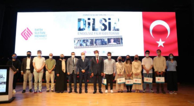 Öğrenciler Engelsiz Bir Yaşam İçin El Ele Verdiler Bir tiyatro sahnesinde çekilen fotoğrafta, barkovizyona yansıtılan görselde Dilsiz filmi  Engelsiz Film Gösterimi yazıyor. Sahnedeki kadınlar ve erkekler yan yana durmuş, objektife bakıyor.
