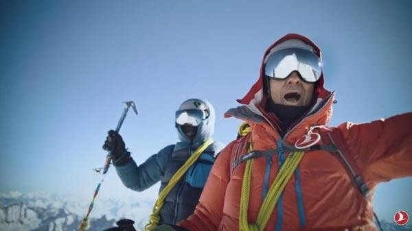 THY'nin Yeni Reklam Filmi Zirve Yayımlandı THY reklamına ait görselde Millî Dağcı Necdet Turhan, arkasındaki dağcıyla zirvede. Görselin sağ altında stilize edilmiş beyaz yaban kazı figürlü THY logosu bulunuyor.